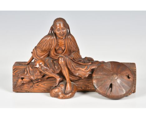A Japanese carved boxwood okimono of an elderly woman seated upon a log, 19th century, dressed in long, flowing robes, her fe