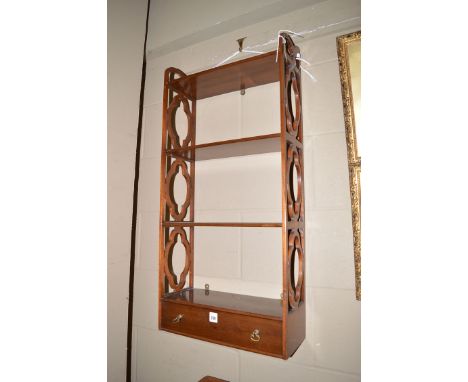 A reproduction mahogany wall hanging four-tier shelf unit, with decorative pierced sides and a shallow drawer in the base.