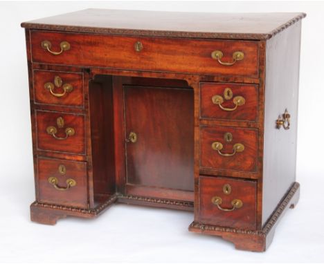 A George III carved mahogany knee hole desk, the top with a rounded edge and carved with ribbons and flower heads, over one l
