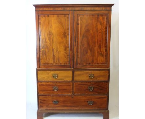 A George III mahogany and boxwood line inlaid linen press, with two panelled doors enclosing five oak press trays, above four
