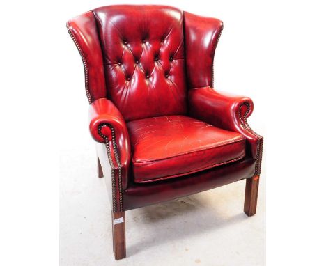 A 20th Century faux leather Chesterfield style wingback armchair in oxblood. Having button back design to backrest and stud d