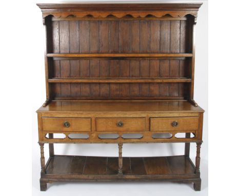 A 19th century oak dresser. The shaped pelmet above two open late shelves, the lower section with three drawers with ring han