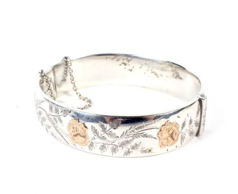 A vintage silver hollow hinged bangle. Engraved with scrolling foliate leaves and gilt highlighted rose flower-heads, hallmar