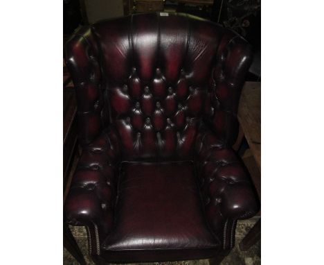 A WINE HIDE UPHOLSTERED LIBRARY WING CHAIR with deep button upholstered back and seat with loose cushion and scroll arms on s