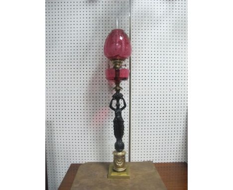 A FINE GILT BRASS FIGURAL OIL LAMP with ruby etched glass shade and reservoir raised on a cylindrical base moulded in relief 