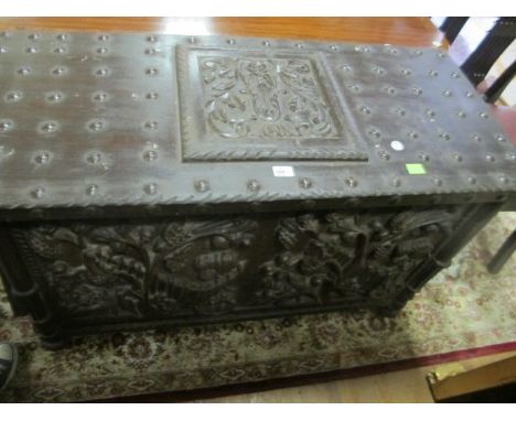A STAINED WOOD CARVED TRUNK the rectangular hinged lid with carved panel and metal studs the frieze carved in high relief wit