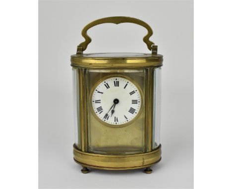 A late 19th century brass cased carriage clock of oval design having a white enamel dial with Roman numerals and raised on fo
