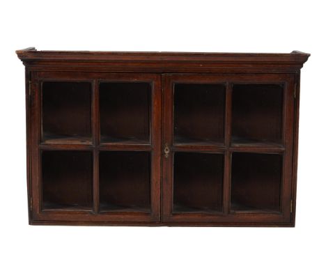 A George II oak hanging wall cabinet, mid 18th century, the moulded cornice above a pair of glazed doors, opening to a shelve