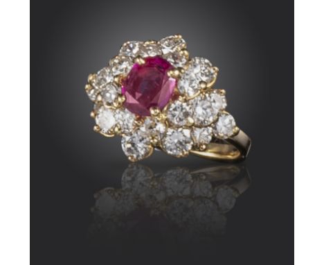 A ruby and diamond cluster ring, of flowerhead design, centred with an oval-shaped ruby within a surround of round brilliant-