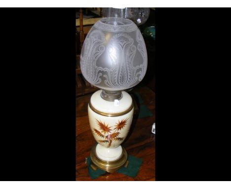 A blush ivory ceramic oil lamp with thistle decoration, and acid etched glass shade