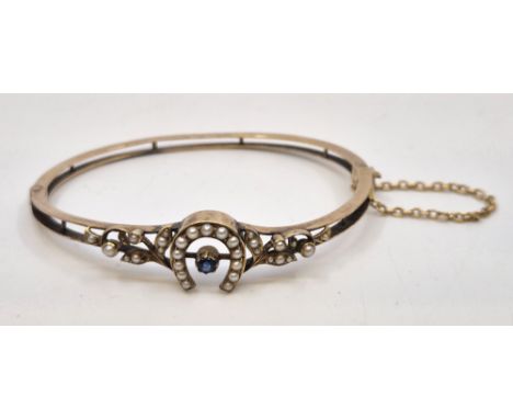 A precious yellow metal, sapphire and seed pearl hinged bangle, of elliptical form, the front half with seed pearl set horses