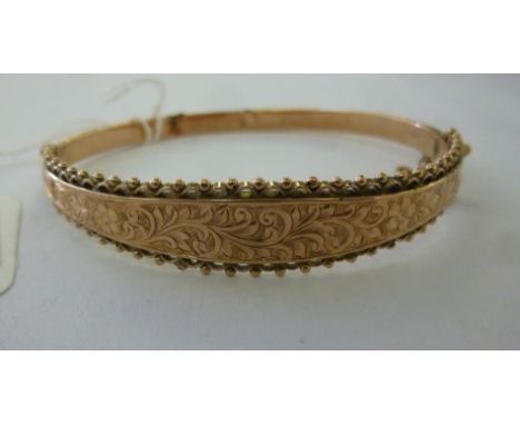A 9ct gold hinged bangle, on a safety chain, decorated with floral and foliate engraving within a beaded wire border        1