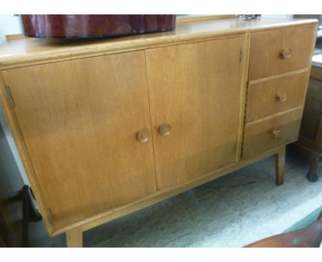 A 1960s light oak finished sideboard, the top having a bar back, over a pair of full height doors and three adjacent deep dra