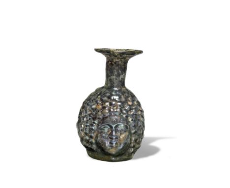  A Roman green glass janiform head flask Circa 3rd Century A.D.The body blown into a two-part mould, with two similar cherubi