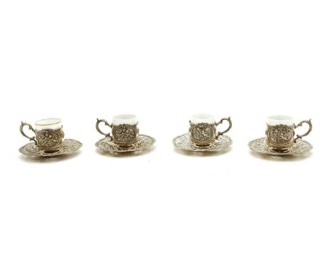 A set of German silver coffee can holders and saucers, decorated in relief with scenes of putti within cartouches with floral
