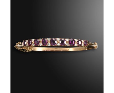 A Victorian ruby and diamond-set hinged bangle, set with graduated cushion-shaped rubies, each separated by a pair of old-cut