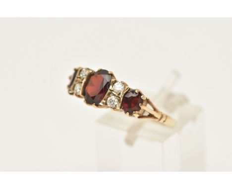 A 9CT GOLD GEM SET RING, set with three graduated oval cut garnets, interspaced with four small colourless cubic zirconia, to