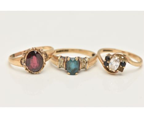 THREE GEM SET RINGS, the first an oval garnet in a scroll and beaded setting, unmarked, the second a central blue topaz and d