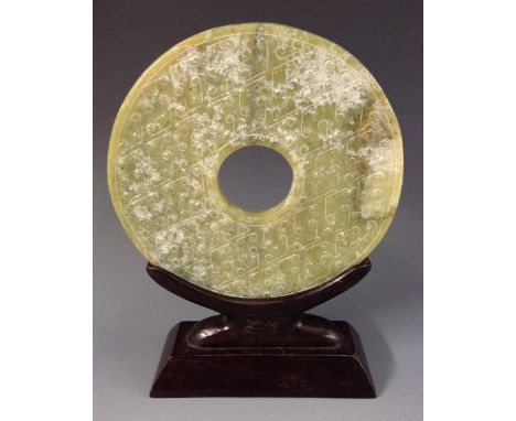 A Chinese jade bi or disc, carved in the archaic manner, 13.7cm diam, hardwood stand 
