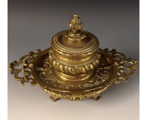 A 19th century brass inkwell, hinged cover, the shaped oval base pierced and cast with leafy scrolls and strapwork, outswept 