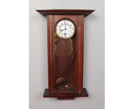 A Mahogany cased 8 day wall clock with pendulum and twin weights. Comprising of a glass fronted door and black Arabic numeral