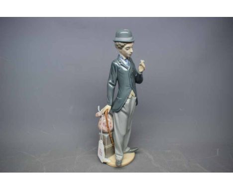 Lladro model of Stan Laurel with suitcase and walking stick, holding a flower, 11ins tall 