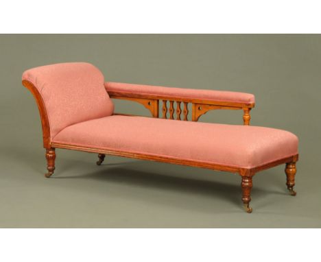 A Victorian oak chaise longue, upholstered in pink foliate patterned material and raised on turned legs with ceramic castors.