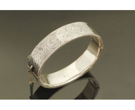 A silver foliate engraved bangle, with safety chain.