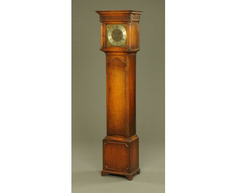 An oak grandmother clock, with moulded cornice above a blind fretwork frieze in turn above a three quarter length trunk door 