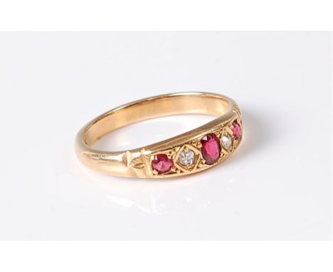 A ruby and diamond ring, the central oval ruby set to either side with a small single cut diamond and a small round ruby, wit