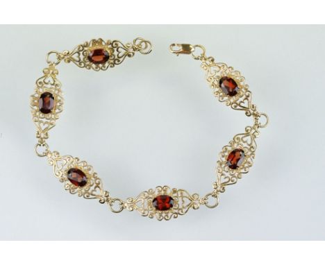 9ct gold and red stone bracelet having scrolled fret work links with an oval cut red stone to each. Marked 9k to lobster clas