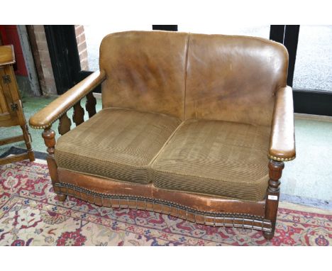 A 1930's oak and leather two seat sofa, padded leather back and arms, squab cushions, serpentine dentil apron, turned feet.