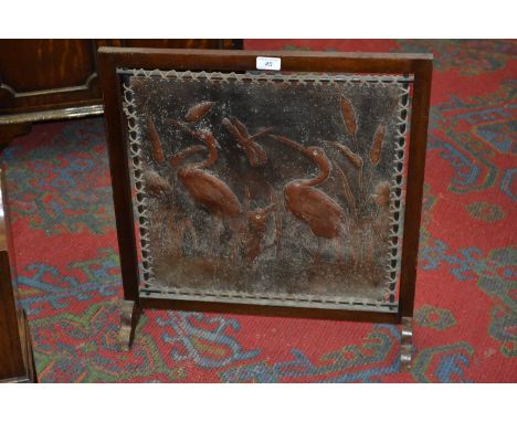 An Art Nouveau mahogany and tooled leather fire screen, embossed with herons amongst reeds and bulrushes, applied glass eyes,