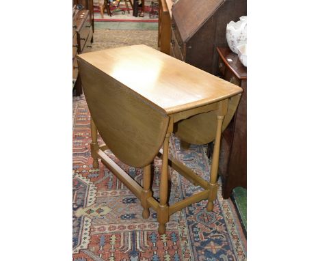 A light oak dropleaf table, oval top, turned supports.