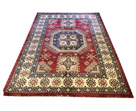 KAZAK CARPET, 260cm x 181cm, central geometric medallion on a ruby field of scattered amulates within multiple geometric bord