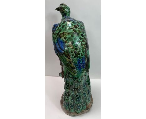A heavy glazed pottery figure of a peacock perched on a gnarled tree trunk in the Chinese style, un marked, 48cms high