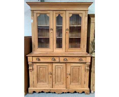 A stripped pine dresser the top with glazed doors enclosing shelves, the base fitted with two short drawers above panelled do