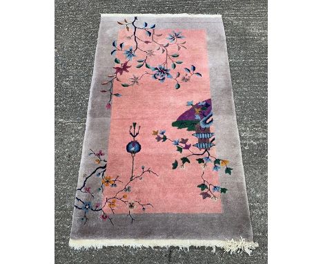 A Chinese wool rug with pagoda, lantern and foliate decoration to the central panel, 153cms x 90cms
