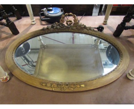 A 19th Century style gilt wood oval wall mirror with ribbon and foliate crest, bevelled glass