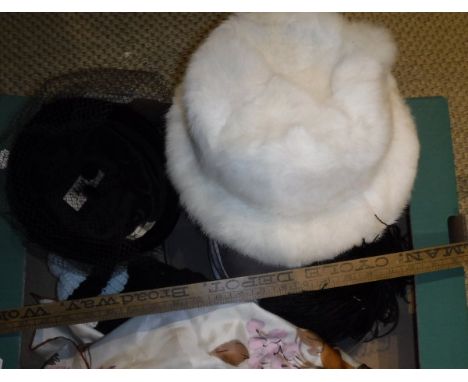 A box containing four hats, to include a black pill box style hat with feather trim and a white fur hat, a vintage wooden mea