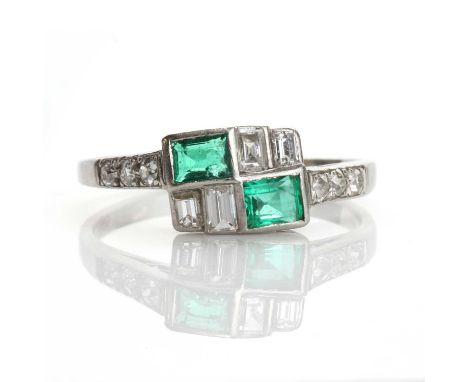 An Art Deco emerald and diamond crossover style ring,with two rectangular step cut emeralds, rub set in diagonal positions. P