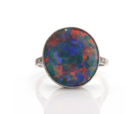 An Art Deco single stone black opal ring, with diamond set shoulders. A circular tallow cabochon cut black opal, milligrain s