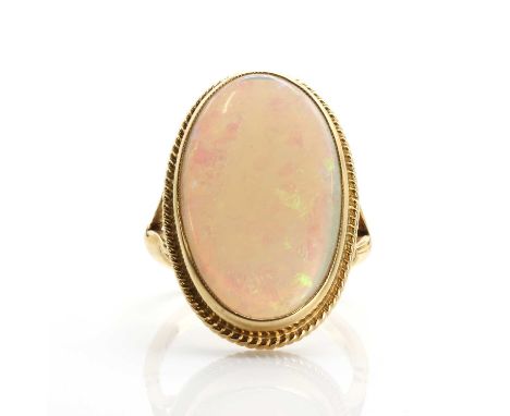 An 18ct gold opal ring,the oval shallow cabochon opal in a rubover collet setting with ropetwist edging, to bifurcated should