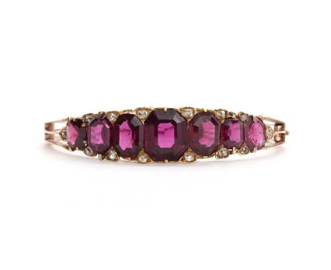A late Victorian almandine garnet and diamond hinged bangle,with seven graduated octagonal step cut garnets, all claw set. Pa