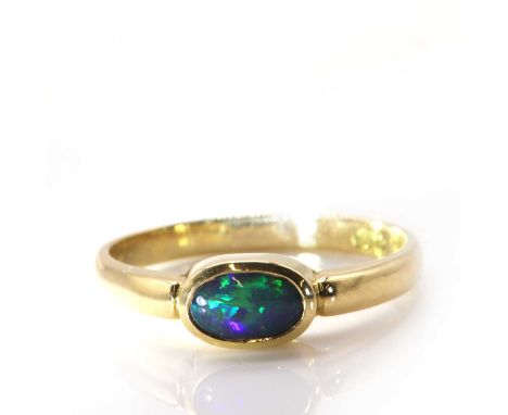 A single stone black opal ring,with an oval cabochon black opal, rub set in a plain collet in a landscape position, with soli