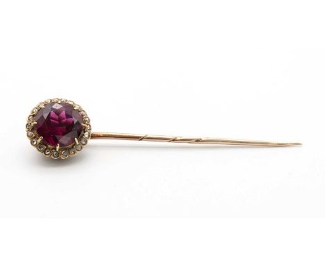 An Edwardian almandine garnet and diamond cluster stick pin,with a circular mixed cut garnet, claw set to the centre. A borde