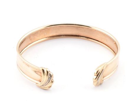 A hallmarked 9ct gold and diamond cuff bangle. The bangle having foliate finials set with a single diamond. Hallmarked Birmin