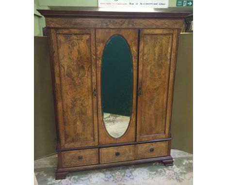 AN EDWARDIAN FIGURED WALNUT WARDROBE having moulded cornice over string lattice inlaid frieze, over an oval bevelled mirror i