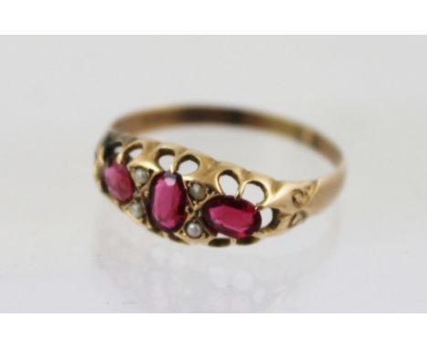 AN EDWARDIAN 9CT GOLD RUBY AND SEED PEARL DRESS RING having three oval rubies and four seeds in tooled setting, size V 