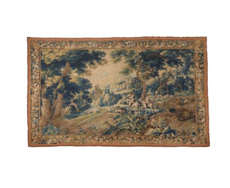 A Flemish verdure tapestry, early 18th century, with two hunters and hounds in a verdant woodland setting, within a floral bo